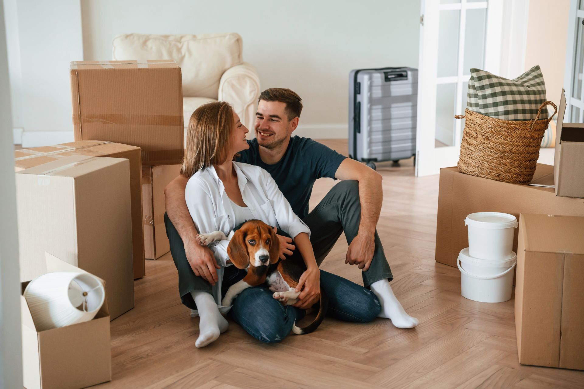 Couple sitting on a floor among moving boxes with a dog in a new home