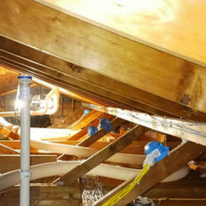 An attic space featuring a slanted wooden roof, a vertical white vent pipe, and several blue electrical junction boxes.