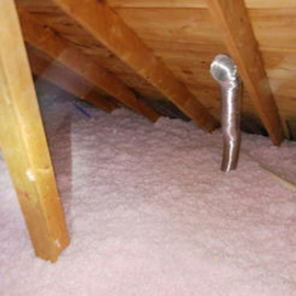 An attic space featuring pink fiberglass insulation covering the floor and a metal ventilation duct rising upright.