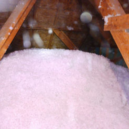 Pink blown-in fiberglass insulation covering the floor of an attic between wooden rafters.