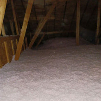 An attic space featuring wooden rafters and joists, with pink blown-in insulation covering the floor.