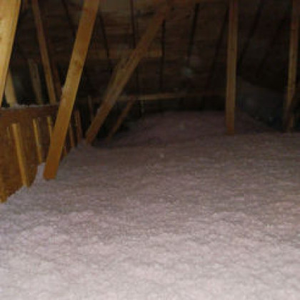 An attic space featuring wooden rafters and joists, with pink blown-in insulation covering the floor.