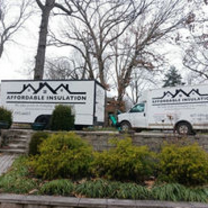 Two white Affordable Insulation work trucks parked on a residential driveway in front of bare trees.