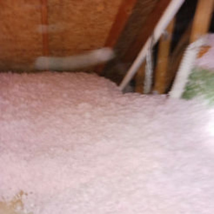 Pink blown-in fiberglass insulation covering the floor of an unfinished attic with wooden rafters.