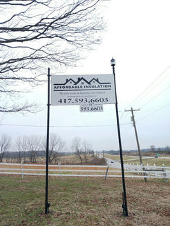 A white sign for Affordable Insulation with a phone number, mounted on two black poles in a field against a cloudy sky.