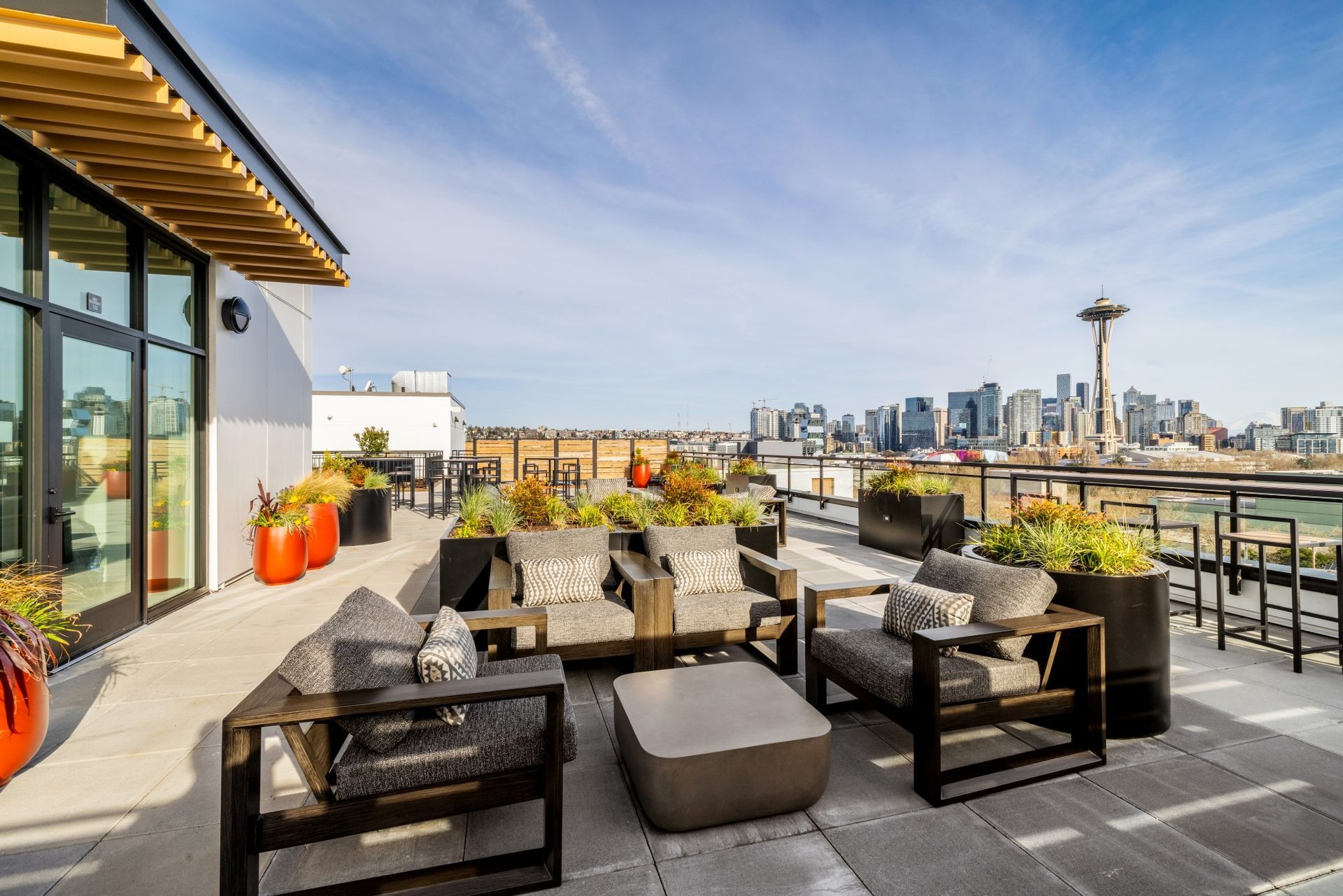 A patio with chairs , tables and potted plants with a view of the city skyline.