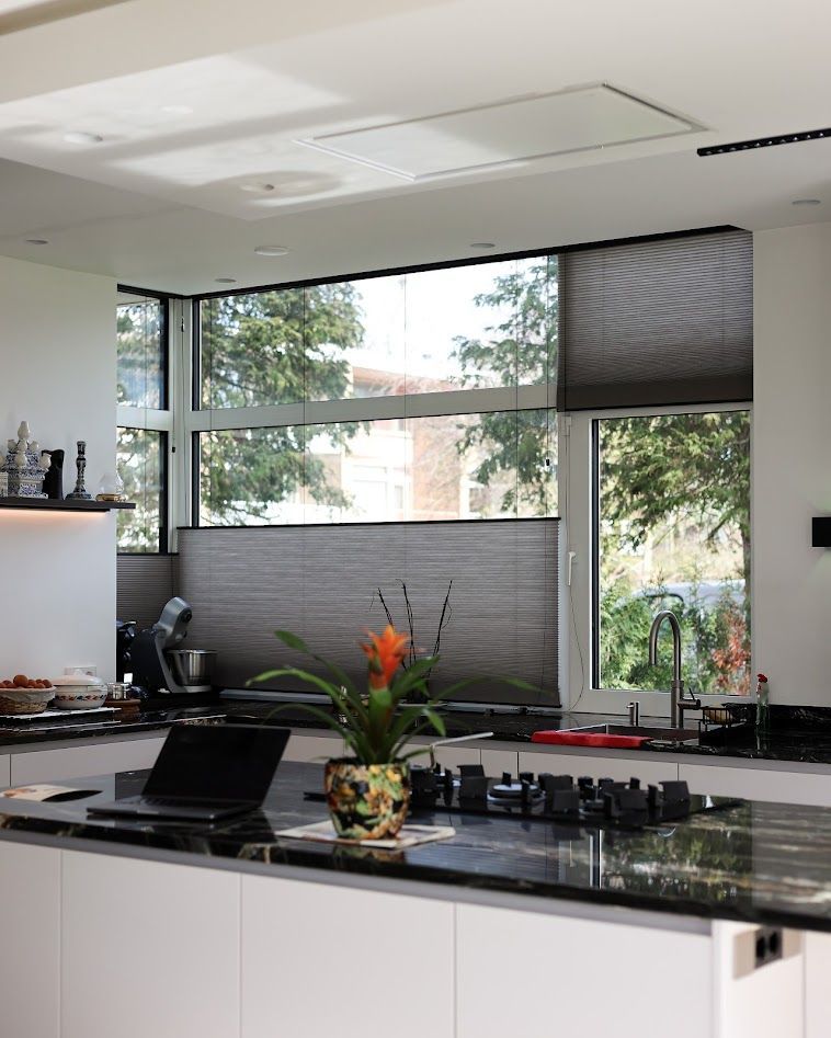Moderne keuken met wit kookeiland, zwart aanrechtblad, grote ramen en een bloemstuk.