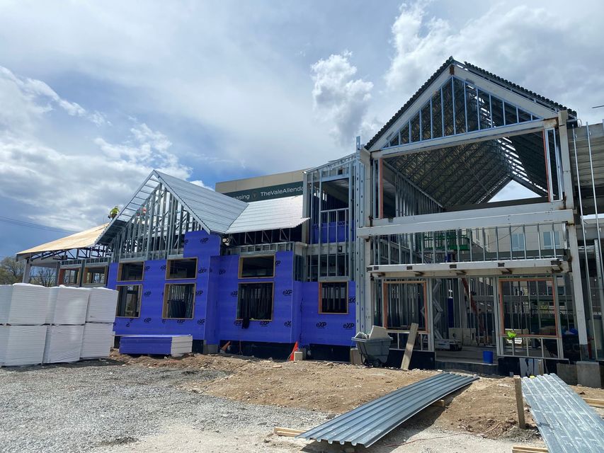 Partially built house with blue sheathing and exposed roof framing under a cloudy sky