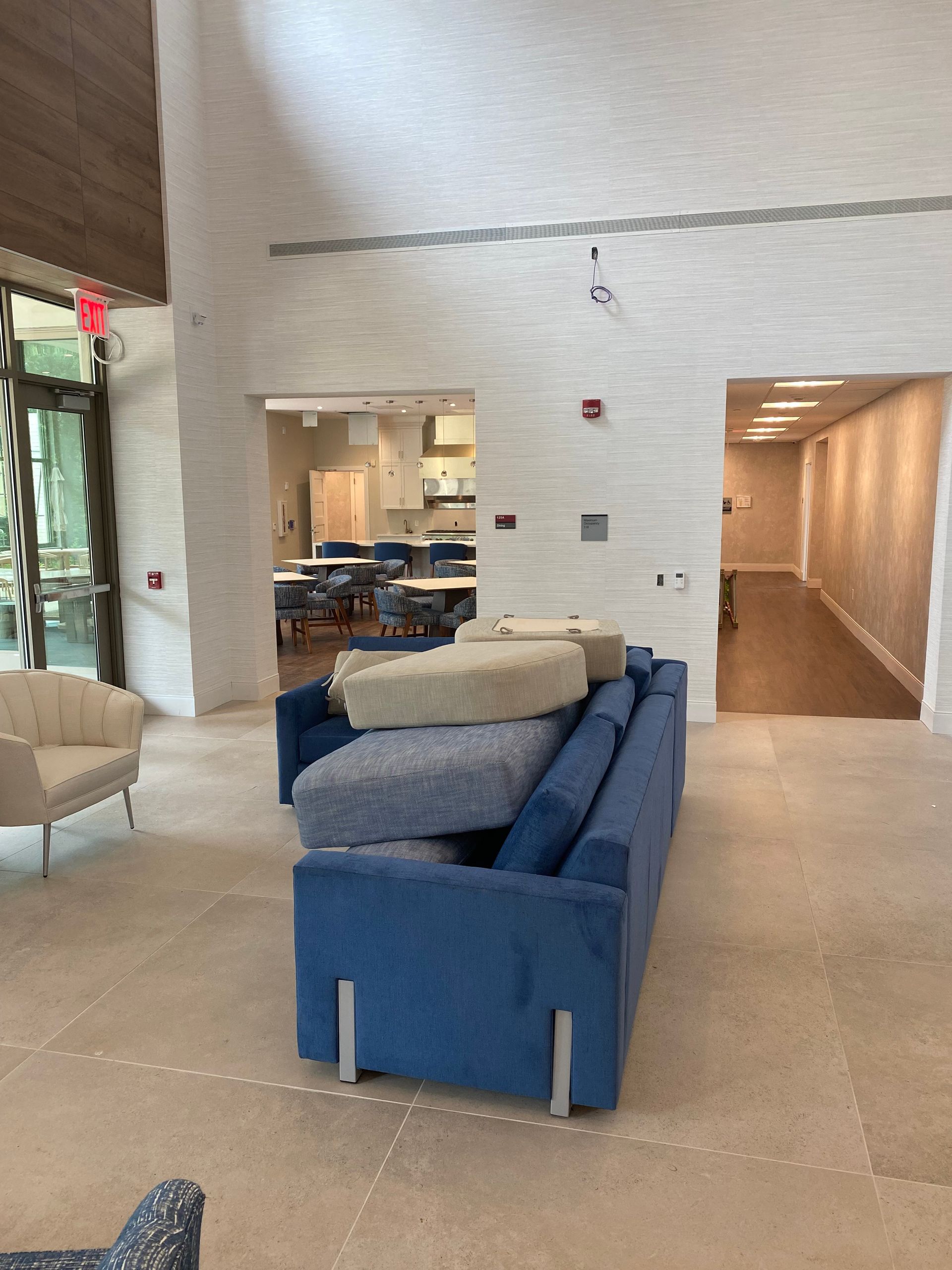 Modern lobby with blue and beige sofas, stone floor, and a hallway to the right