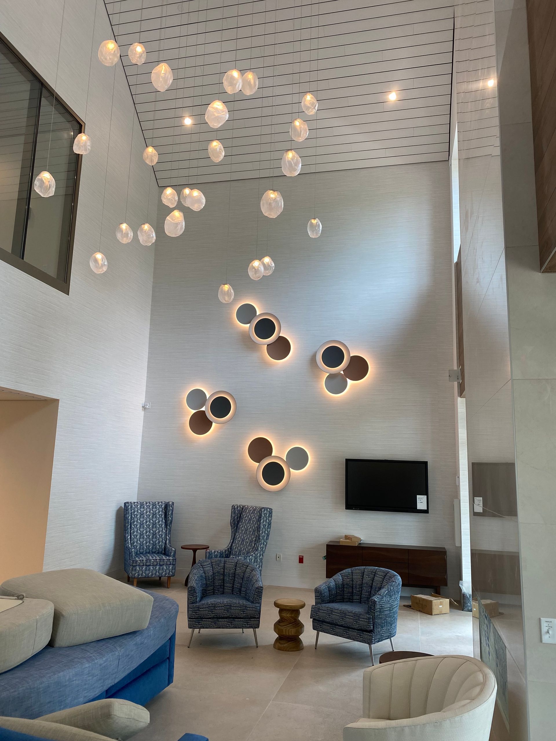 Modern lounge with blue chairs, white walls, hanging globe lights, and wall-mounted TV