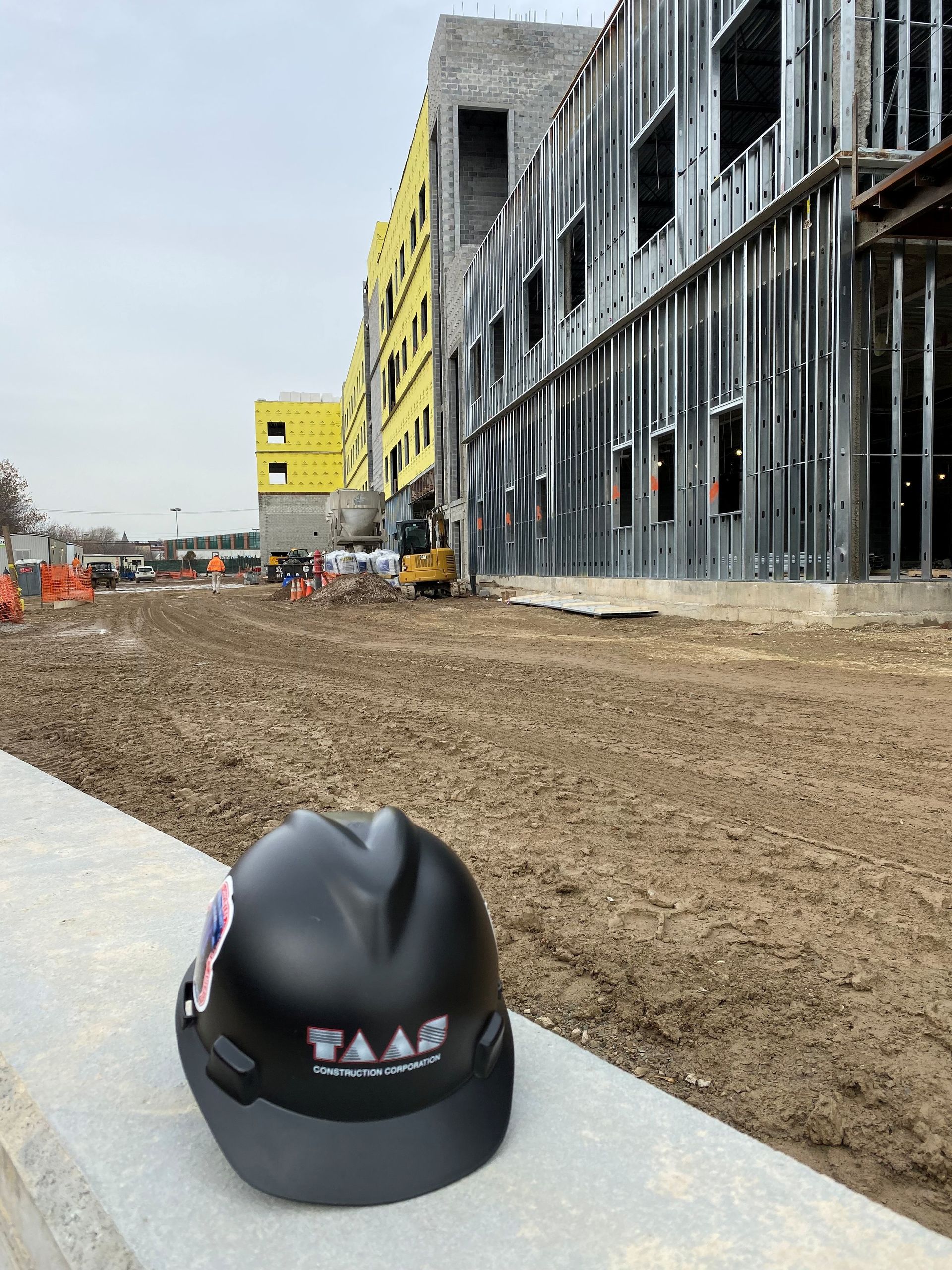 Construction site with a black hard hat on a concrete ledge in the foreground and a building under construction behind it