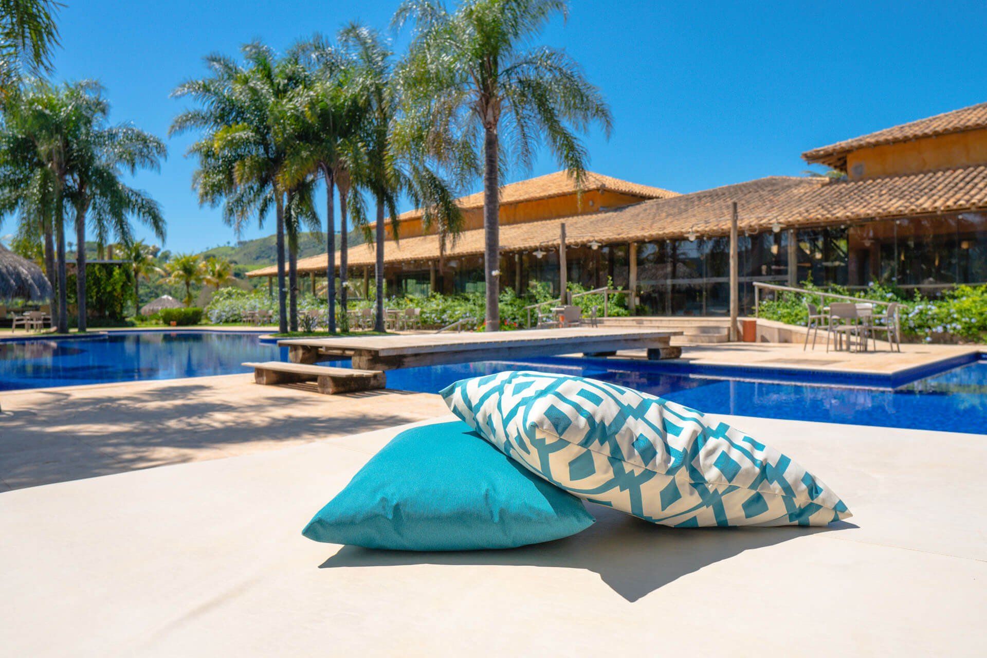 almofadas com piscina e palmeiras ao fundo