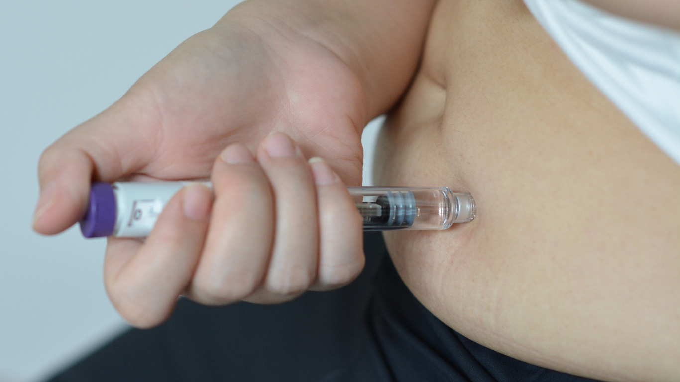 A person self-administers an injection on their stomach
