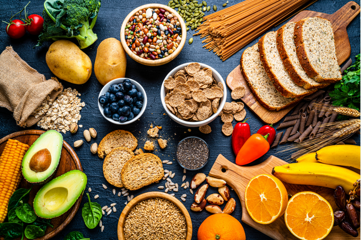 A spread of fiberous foods including seeds, oats, bread, avocados, blueberries, potatos, oranges, beans, cereals, bananas and more