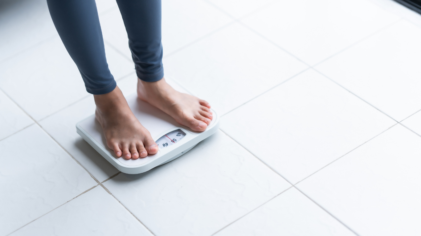 a white scale on tile floor with a person's feet and lower legs standing on it