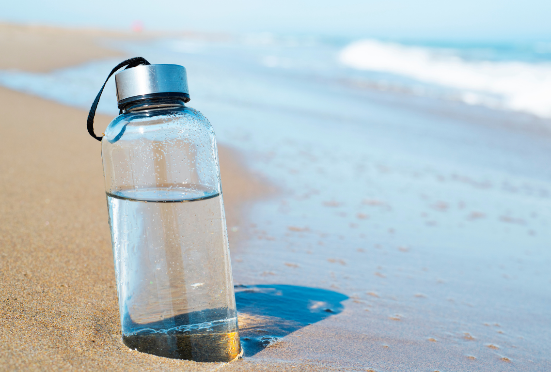 A glass waterbottle sits submerged in the sand on the beach, right at the water's edge