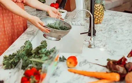 A woman is washing vegetables in a kitchen sink.