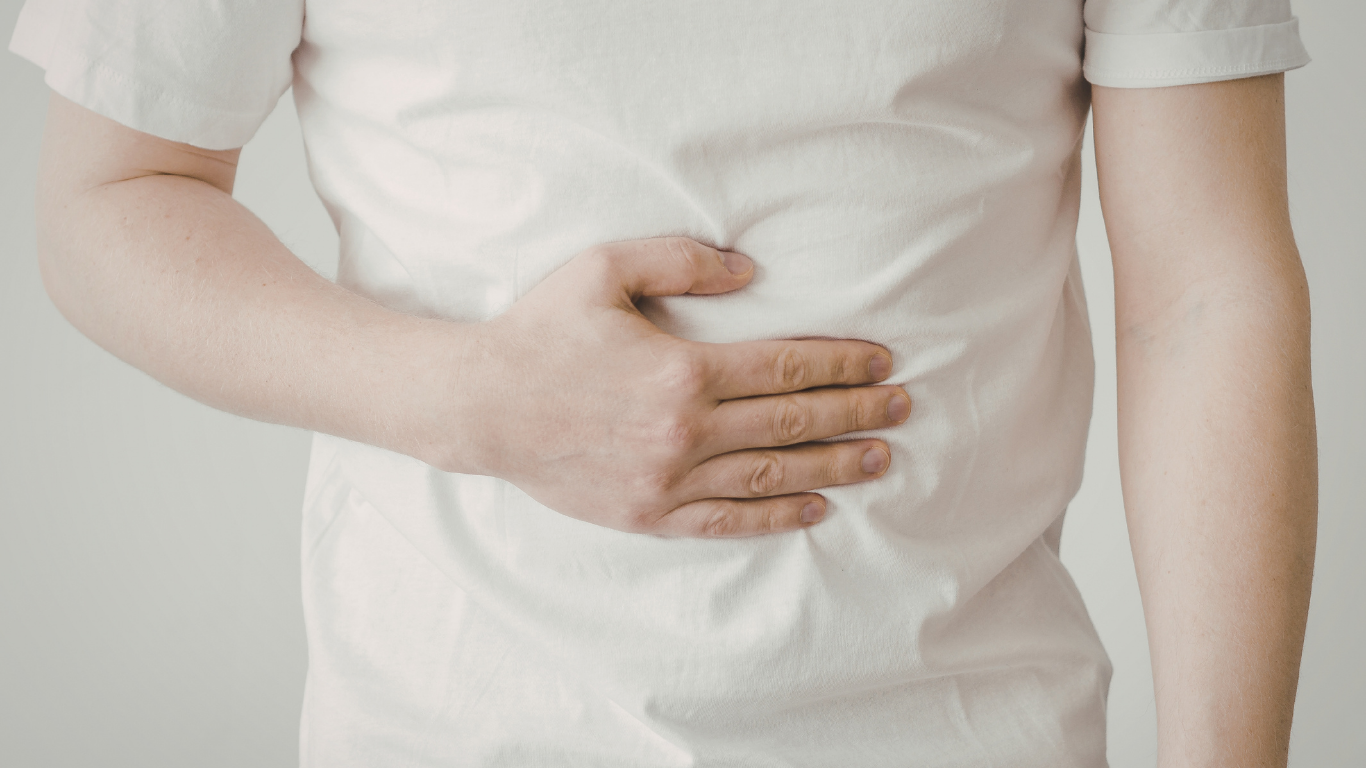 A person wearing a white shift holds their stomach
