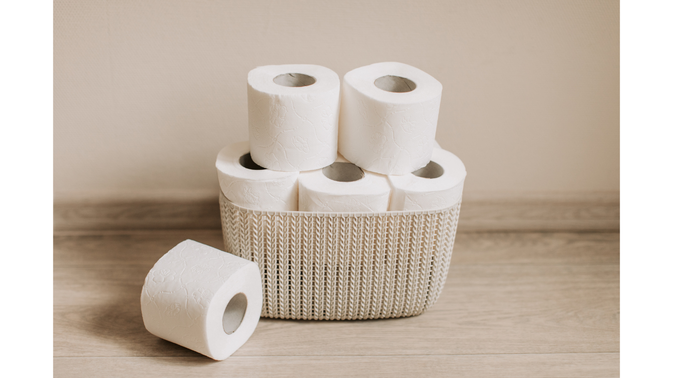 A basket of toilet paper sitting on the ground with one roll out.