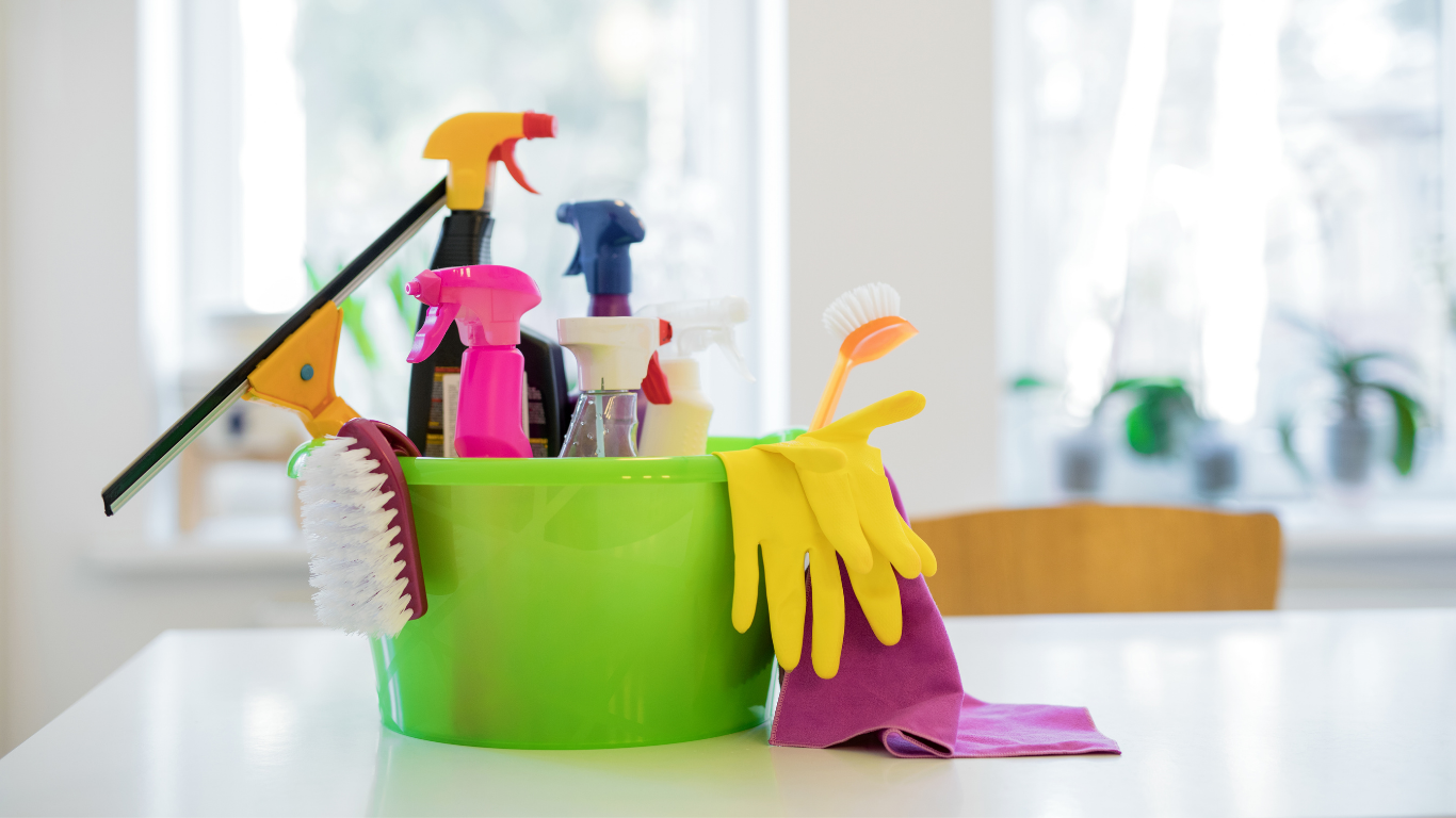 A bright green bucket with cleaning products, brushes, and gloves sits on a countertop.