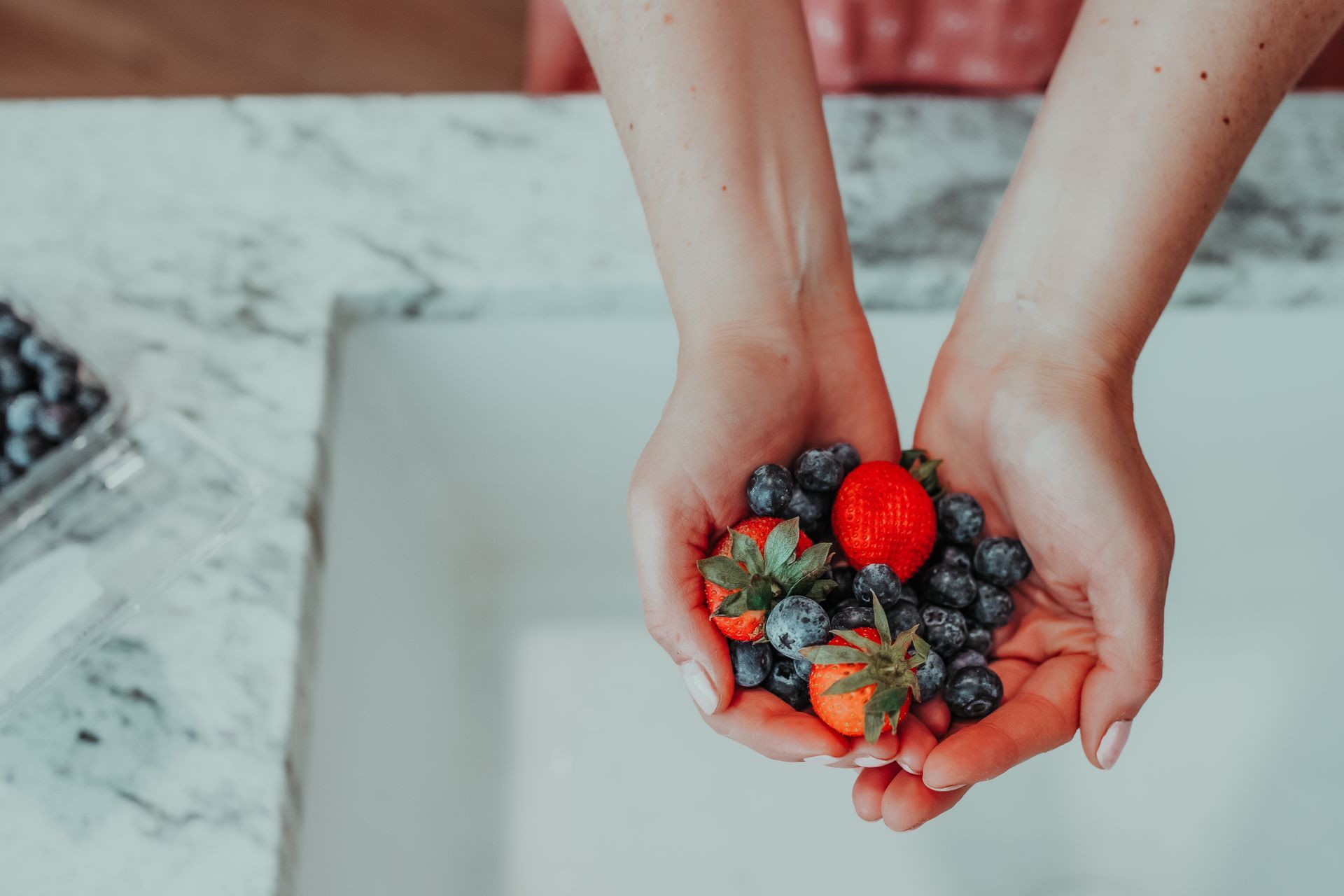 A woman is holding strawberries , blueberries , and raspberries in her hands.