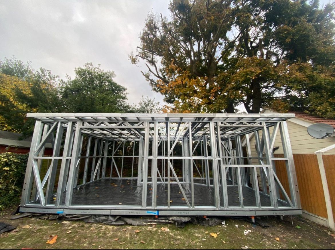 Metal frame of a building under construction, set on a dark foundation, outdoors, with trees in the background.