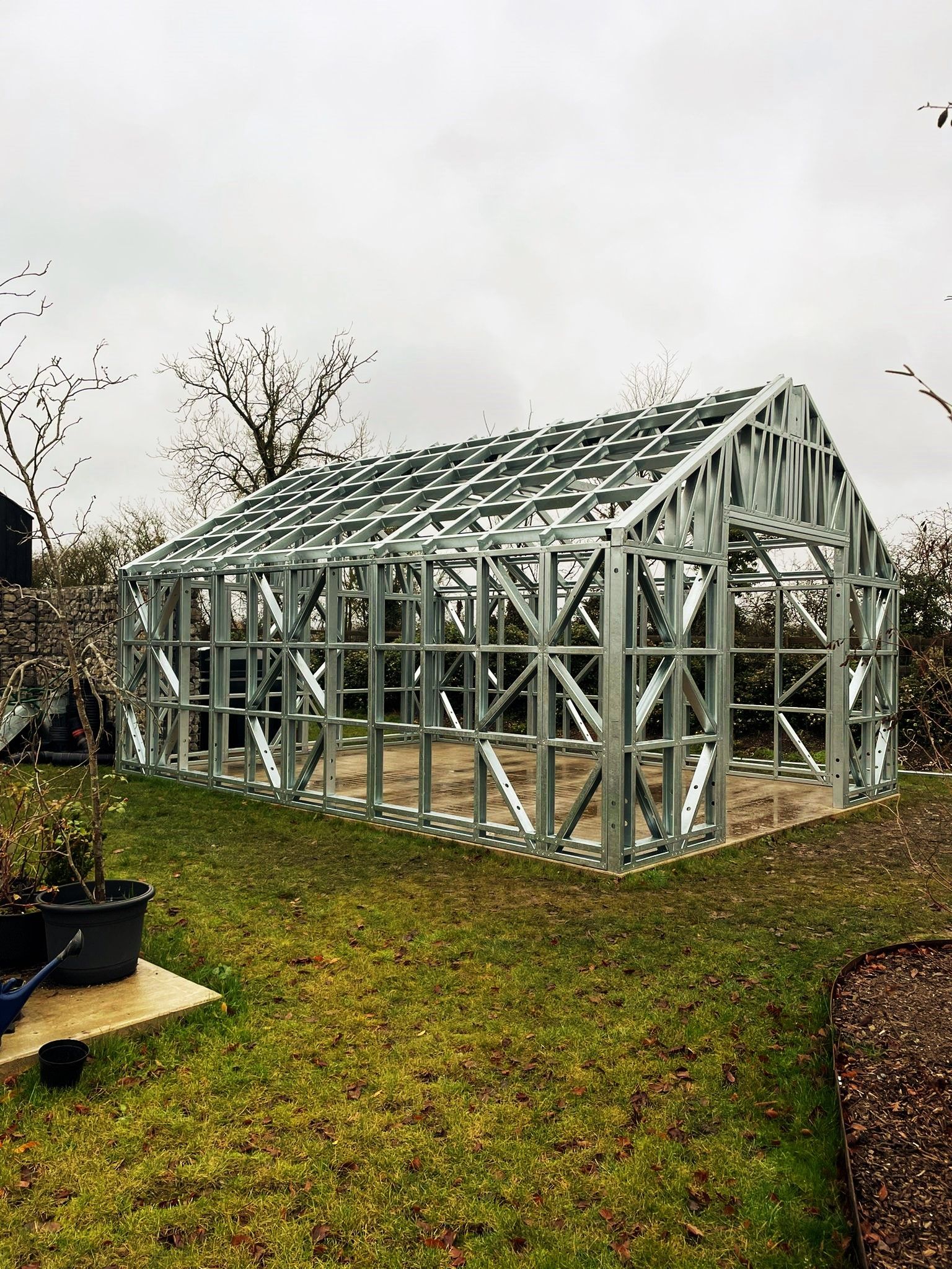 Metal frame greenhouse being constructed on a lawn, overcast sky.
