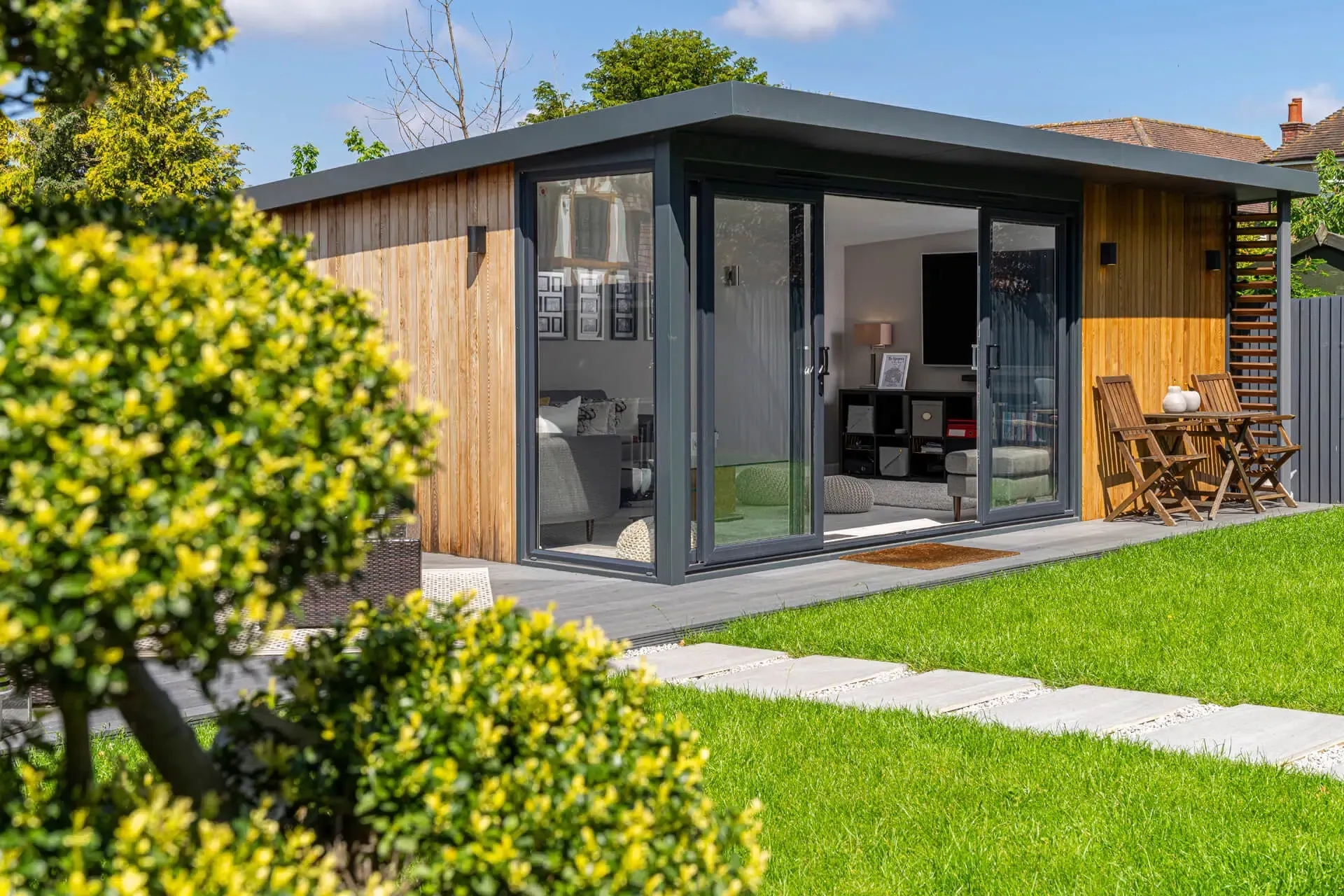 Modern garden office with glass doors, wood siding, and outdoor seating.