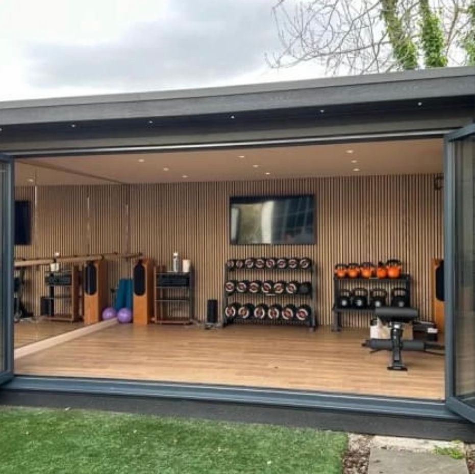Home gym with weights, TV, and open doors. Wooden paneling and floor.