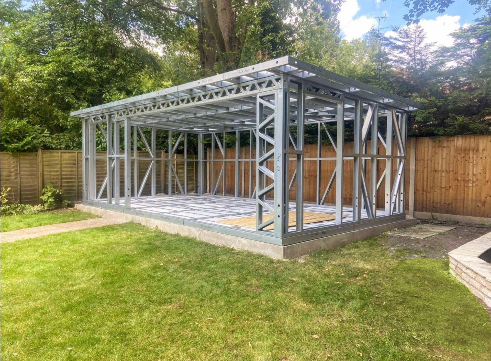 Metal frame of a shed under construction in a grassy backyard, with a wooden fence in the background.