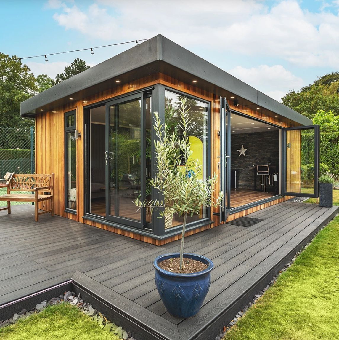 Modern wooden garden room with dark gray deck, glass doors, and a small tree in a blue pot.