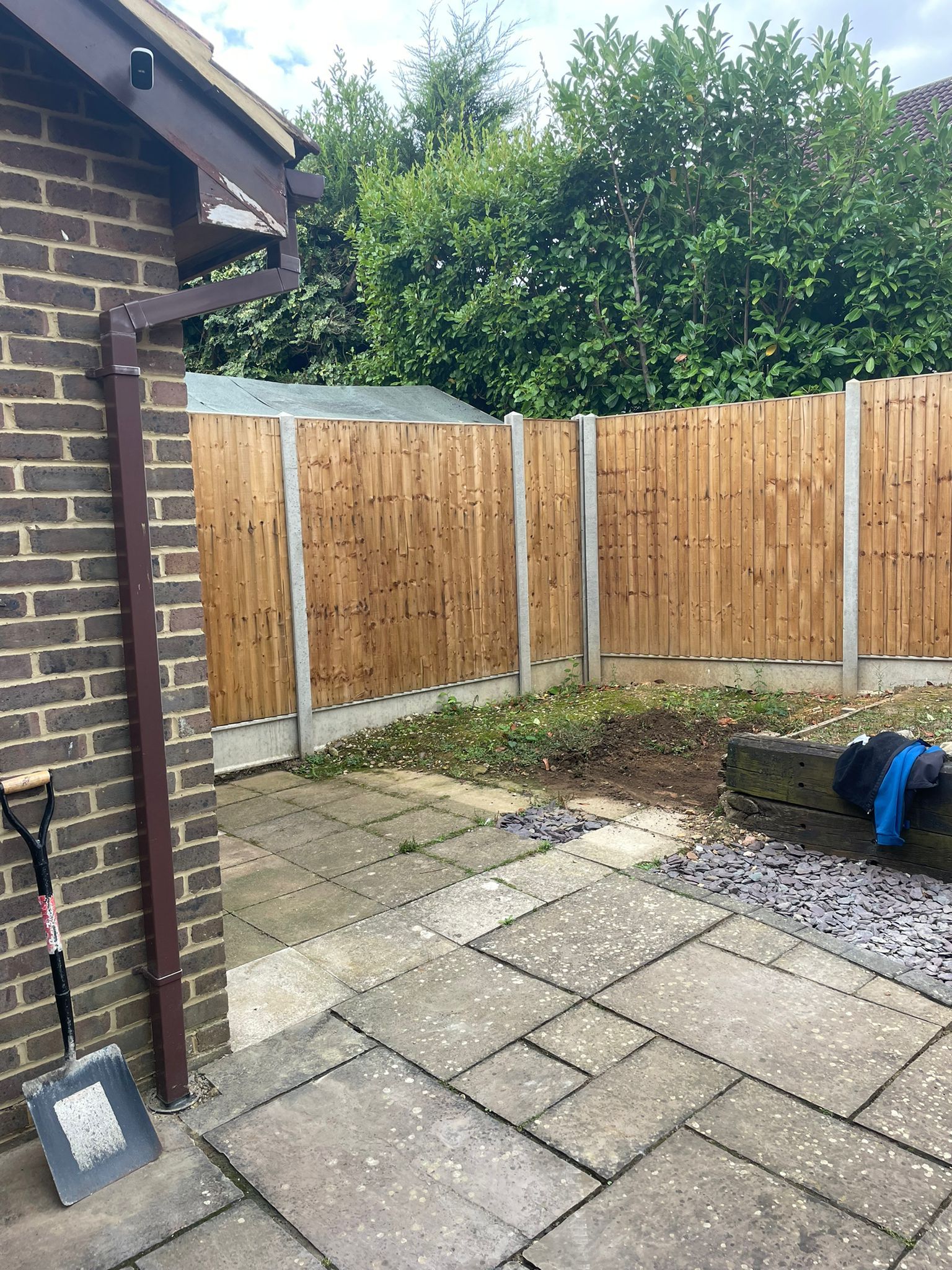 Backyard with brick wall, wooden fence, paved patio, and shovel.