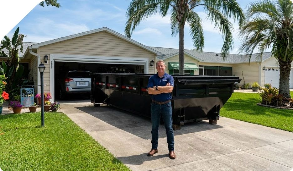 Man standing beside a black trailer in a driveway in front of a garage on a sunny day