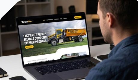Person viewing a laptop displaying a landscaping company website with a yellow truck on the homepage
