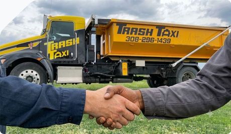 Two people shake hands in front of a yellow Trash Taxi truck