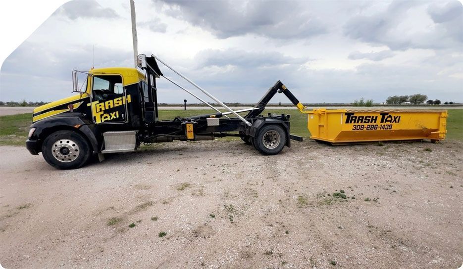 Yellow tow truck with attached trailer parked on a gravel lot under a cloudy sky.