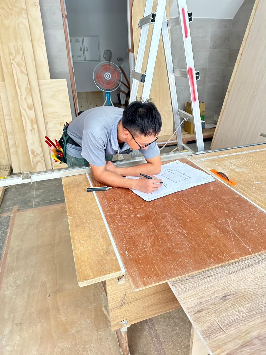 A man is sitting at a wooden table looking at a blueprint.