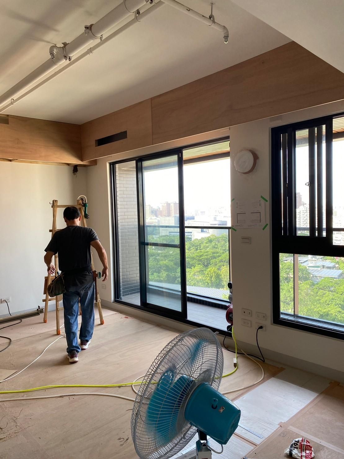 A man is standing in a room with a fan and a ladder.