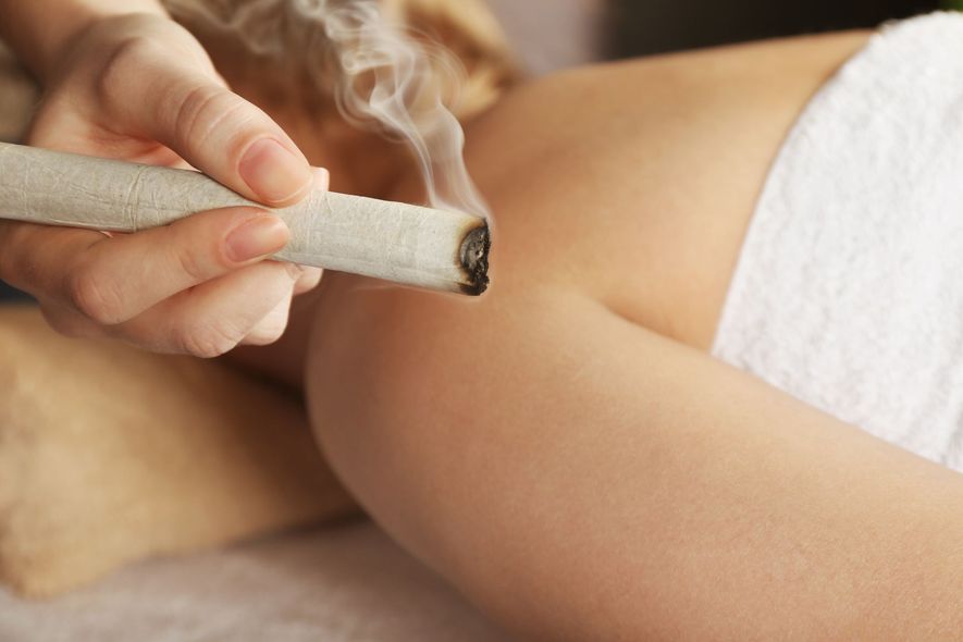 A hand holding a smoking moxa stick near a person's arm, likely for traditional medicine.