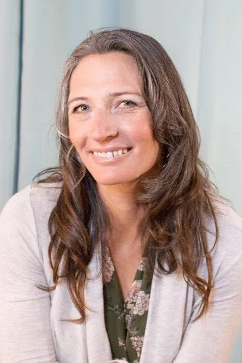 Woman with graying hair smiling, wearing a light cardigan over a floral print shirt.