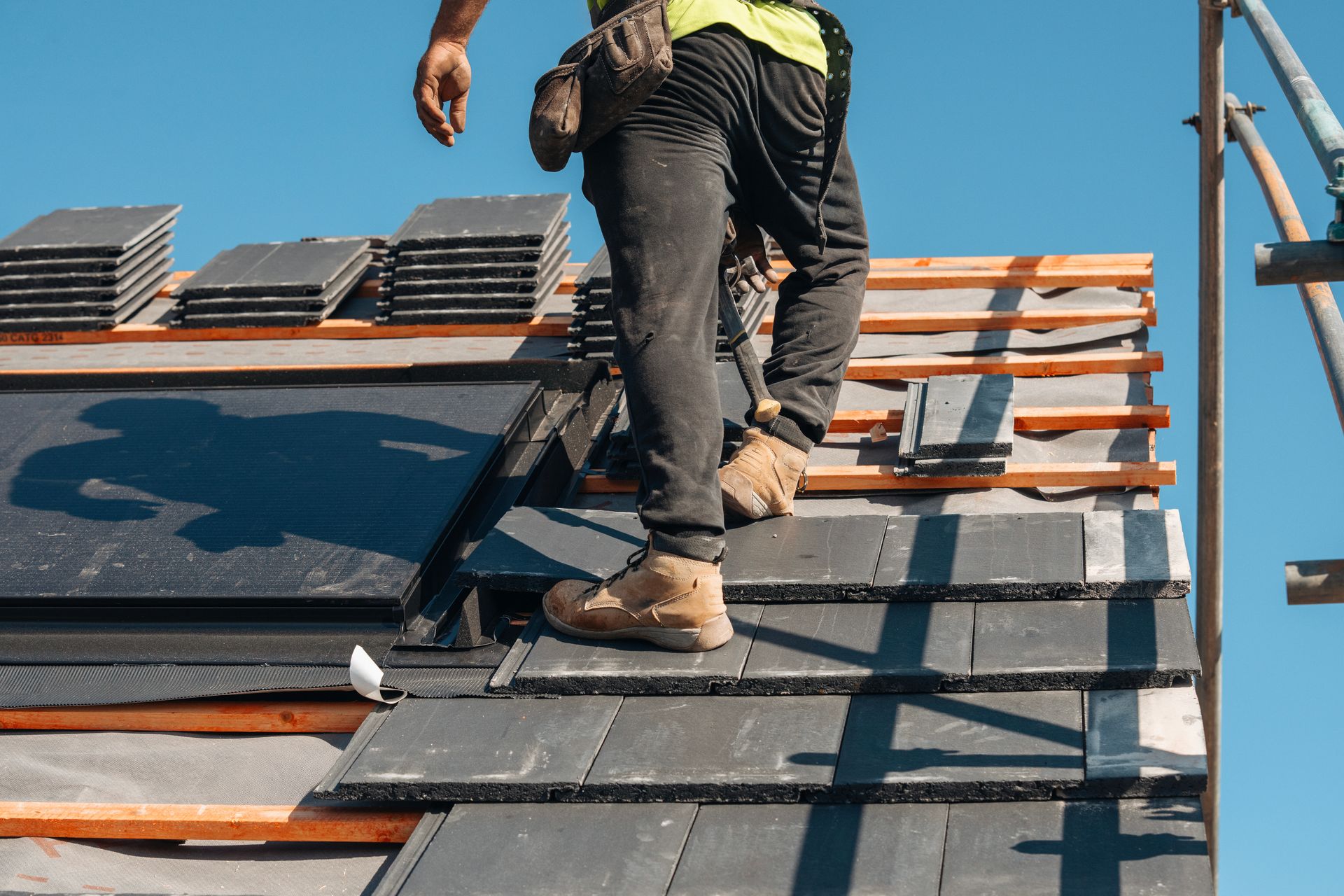 Skilled roofer installing slate tiles on a building under clear blue sky.