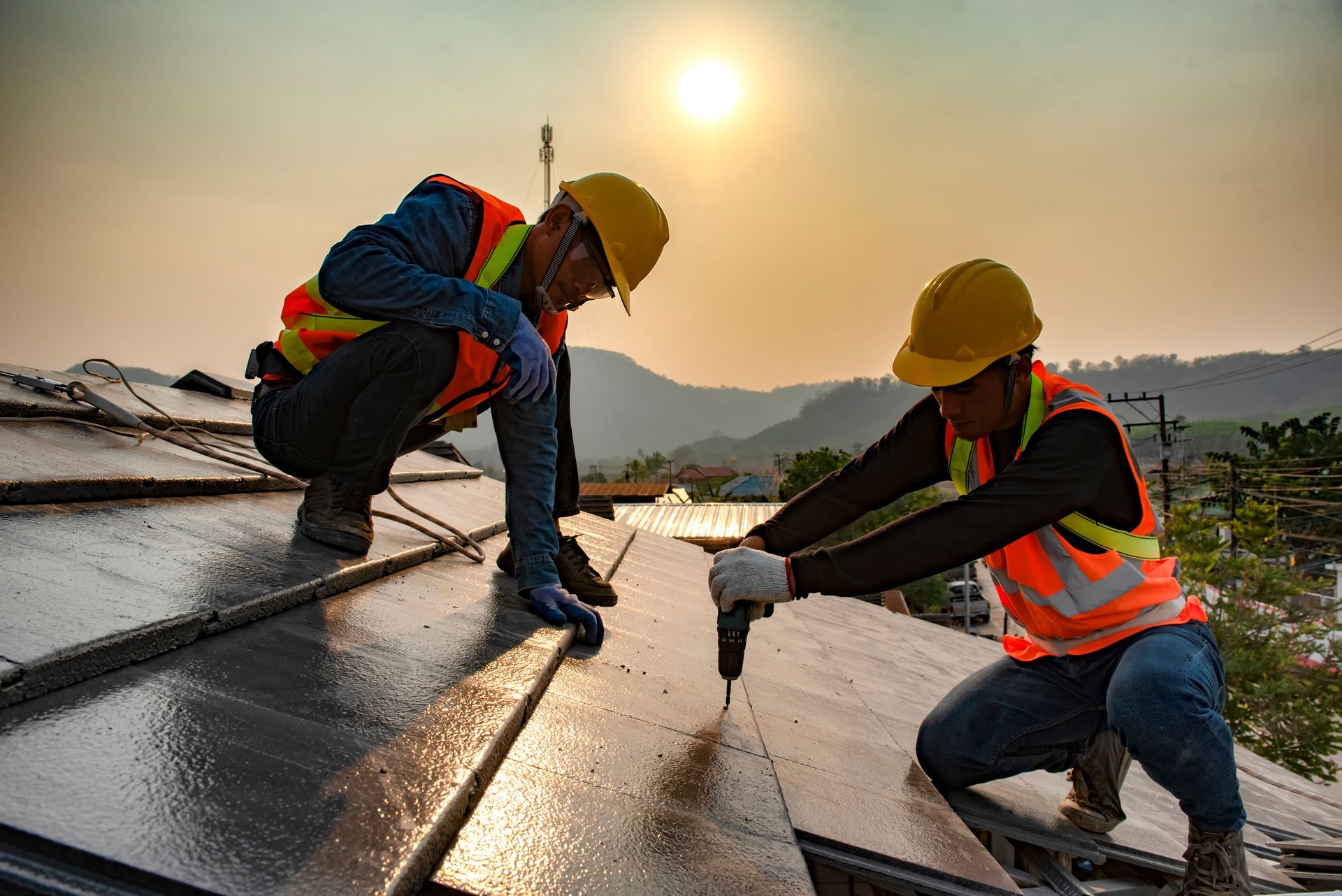 Two construction installing roofing panels during sunset.