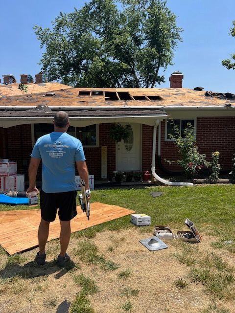 Worker standing in a yard inspecting storm-damaged roof on a brick house
