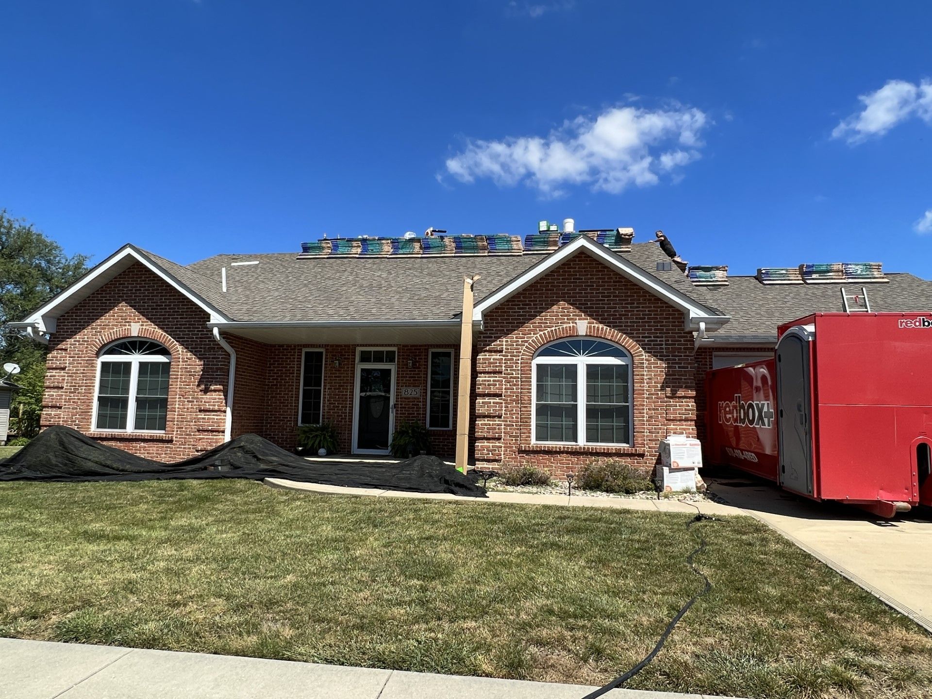 Brick suburban house with white trim, damaged roof, and a red dumpster in the driveway