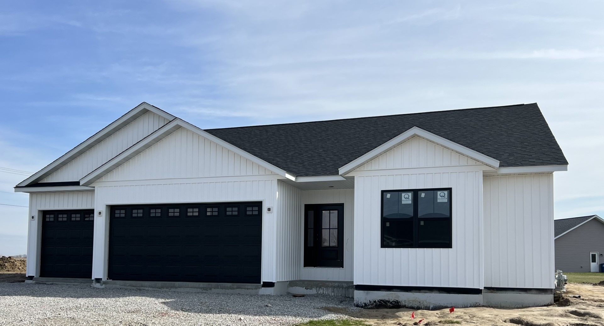 New white single-story house with black roof, garage, and gravel lot under a clear blue sky