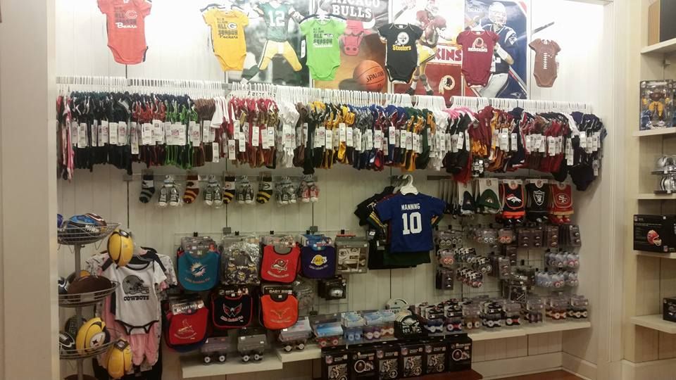 A retail display wall featuring assorted baby apparel and accessories with various professional sports team logos.