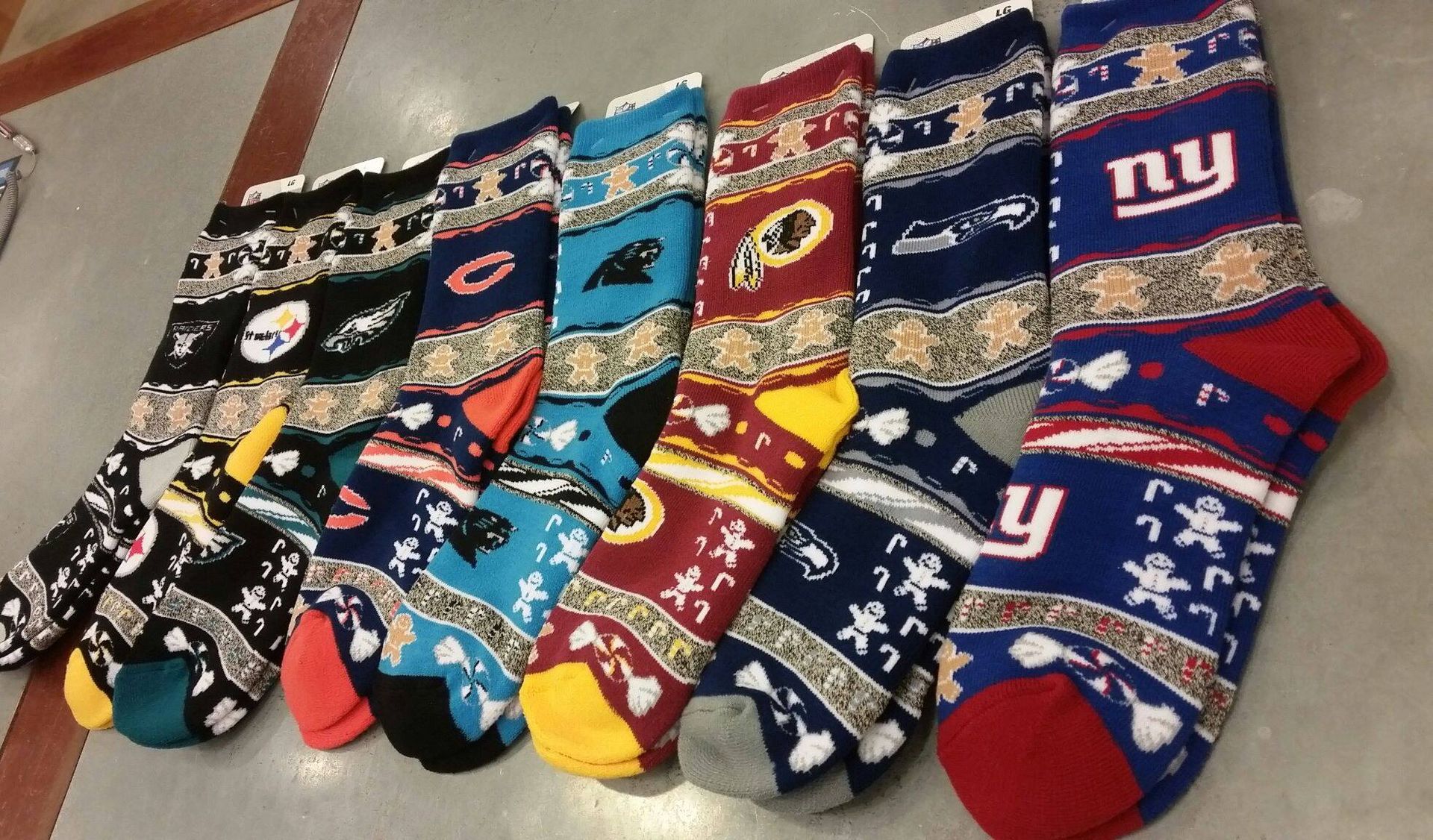 A row of NFL team-themed holiday socks with gingerbread men patterns, arranged side-by-side on a gray floor.