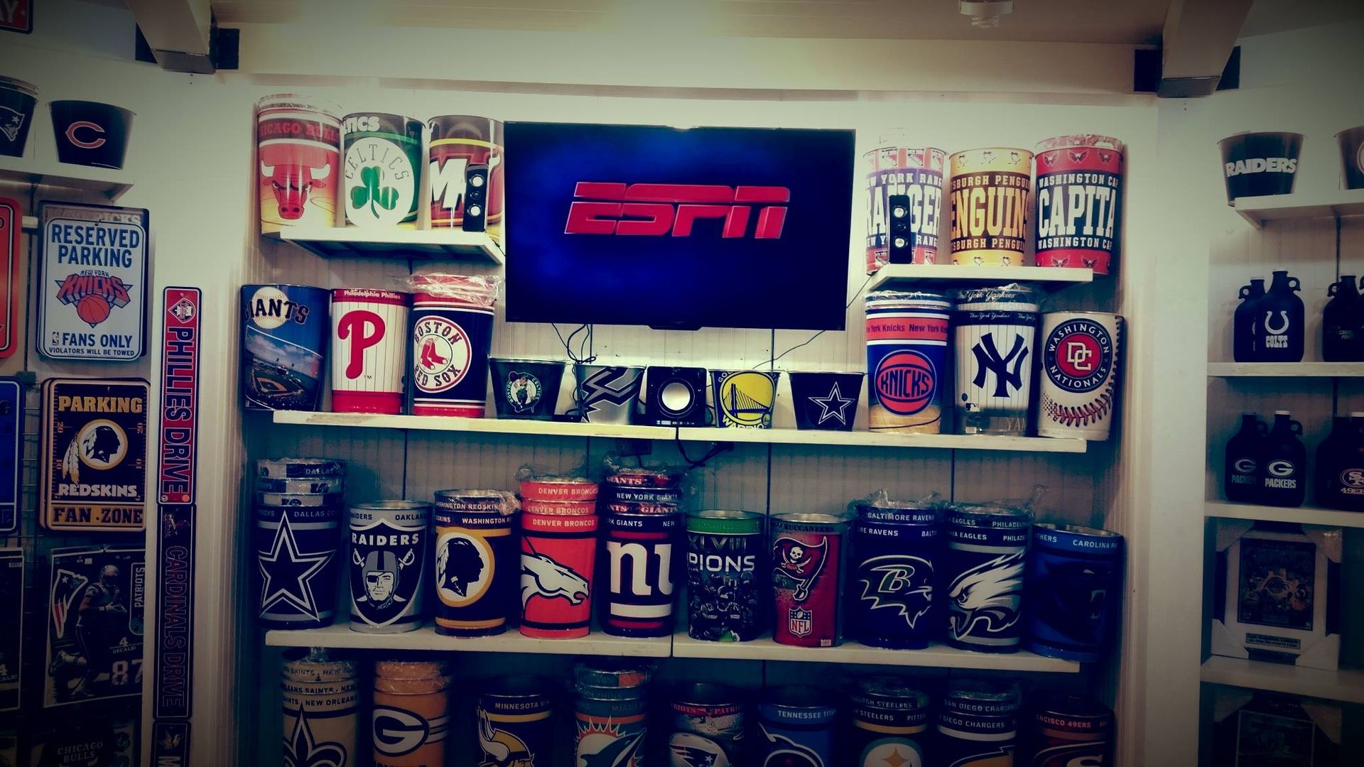 Shelves displaying numerous sports-themed beer cans and memorabilia, with an ESPN logo centered on a wall-mounted TV.