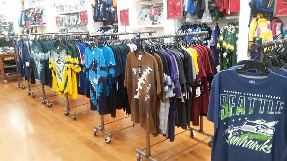 Racks of sports apparel, including jerseys and T-shirts with various team logos, are displayed in a retail store.