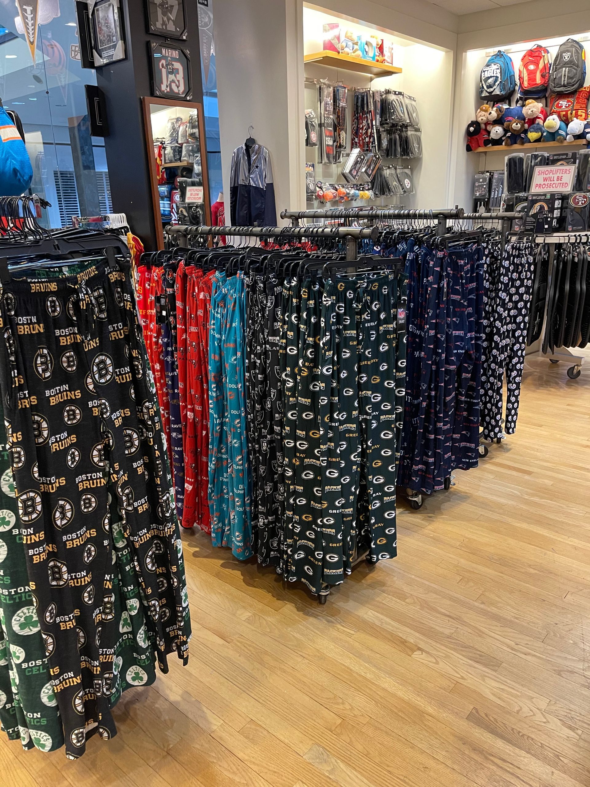 A retail store display featuring rows of colorful patterned pajama pants hanging on racks over a light wooden floor.
